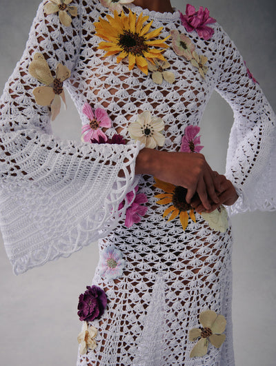 The model wears a white long sleeve crochet dress with pink, yellow, and white flowers embroidered around the dress from fall 2021.