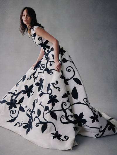 The model is wearing a white gown with black embroidered flowers from Fall 2021.