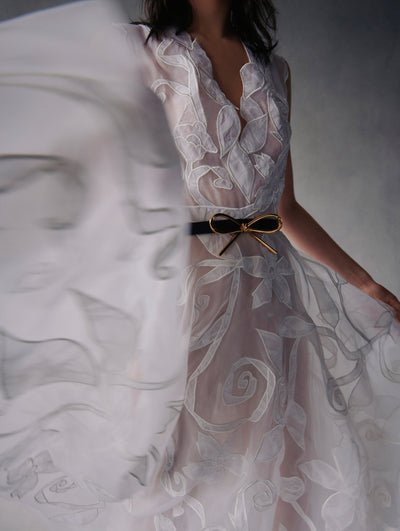 Close up of model wearing a translucent white embroidered dress with a black bow belt around the waist from Fall 2021