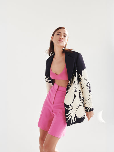 A model wears a pink short and top set with a navy blazer with white pineapples embroidered 