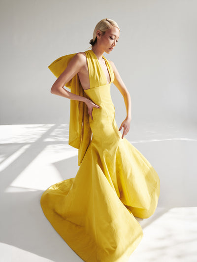 A model wears a long yellow gown with a bow on the back