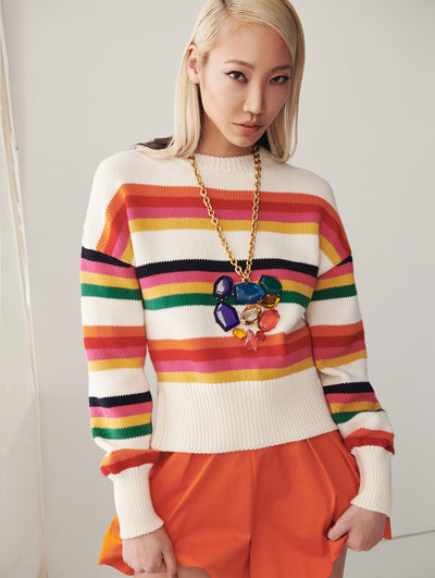 A model wears a rainbow striped sweater with orange shorts
