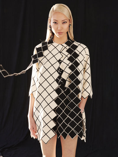 A model wears a black and white coat and shirt with lattice detailing