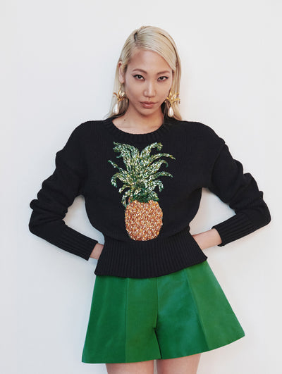 A model wears a black sweater with an embroidered pineapple and green velvet shorts