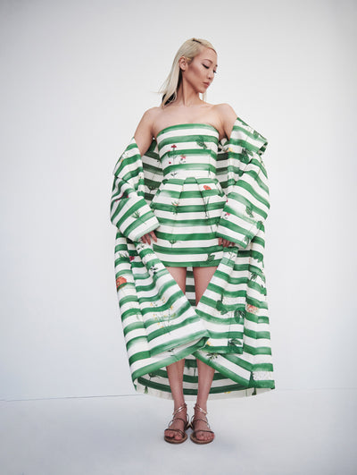 A model wears a short dress and matching jacket with green and white stripes, with flowers printed
