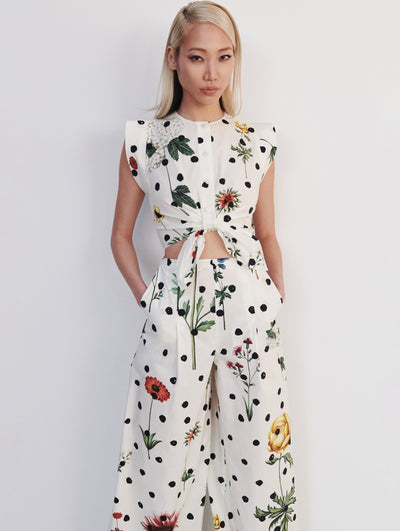 A model wears a shirt and pant set with black dots and flowers printed