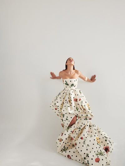 A model wears a long ivory gown with black polka dots with flowers