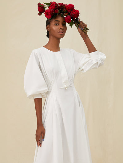A model wears a long white dress and is holding red roses