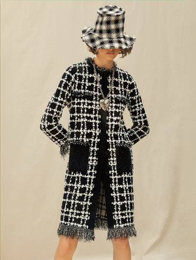 A model wears a long black and white tweed coat with a matching bucket hat