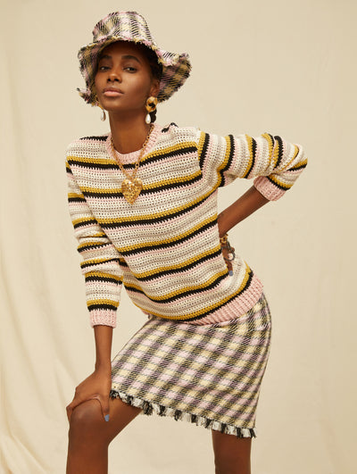 A model wears a striped tweed shirt and skirt set with a matching bucket hat