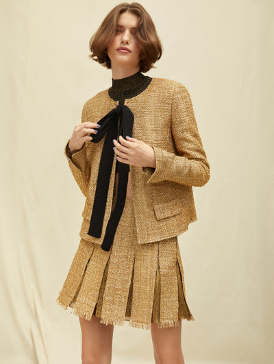 A model wears a gold suit set with a blazer and skirt, a black bowtie in the middle