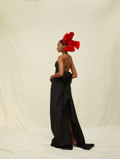 A model wears a long black gown with a large red bow headpiece