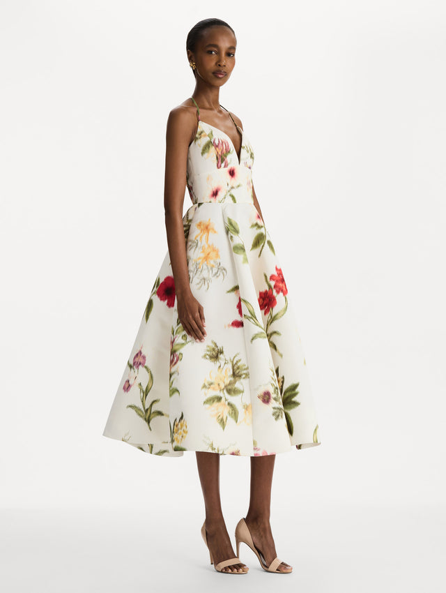 The model is wearing the Chiné Dominican Mixed-Floral Faille Cocktail Dress. Featuring a halter neckline, structured bodice, midi skirt, and belt at waist. Side View.