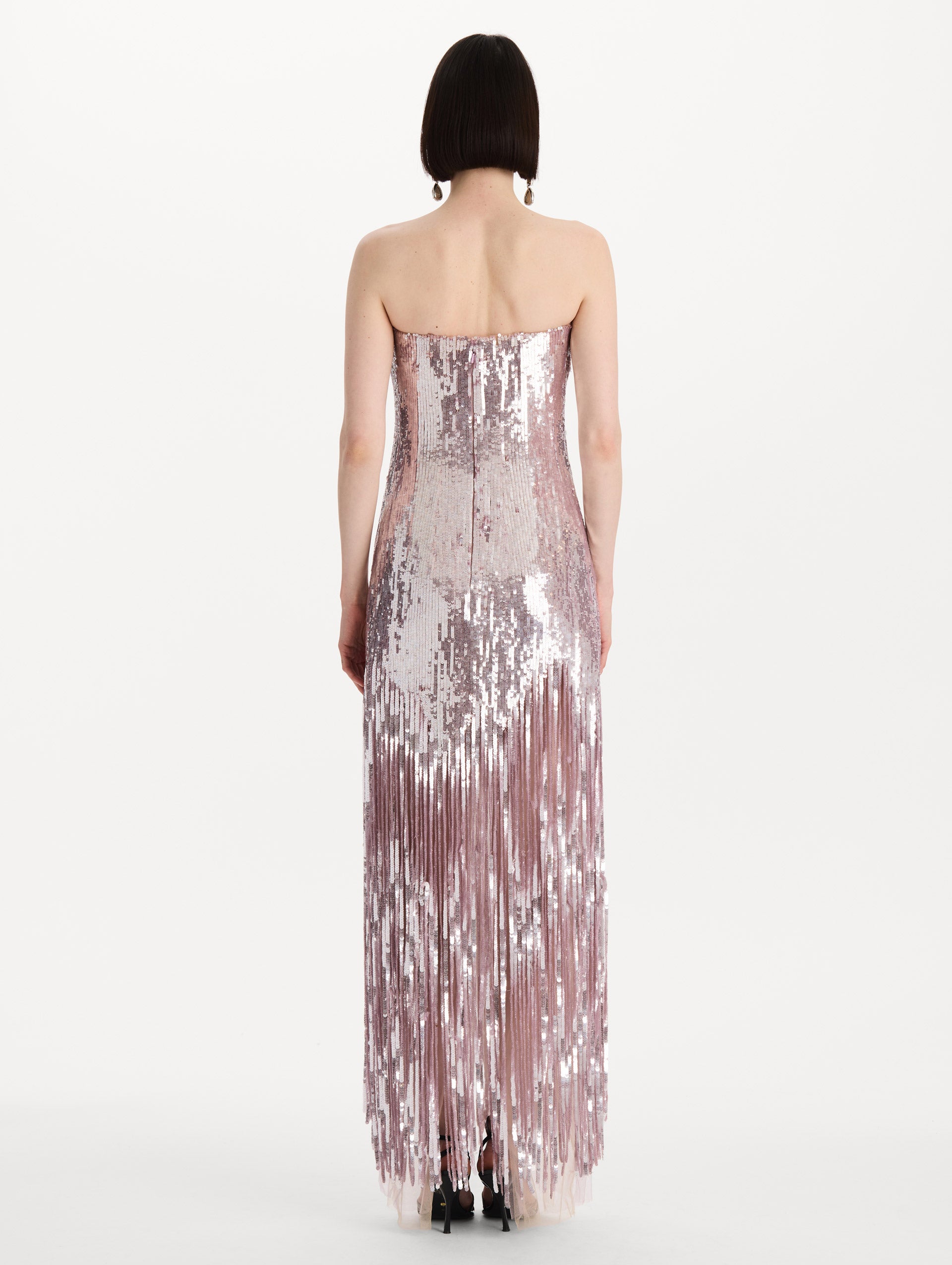 The model is wearing the Sequin Fringe Strapless Gown in the color tulip pink featuring a strapless silhouette, all-over sequins, and fringe skirt. Back View.