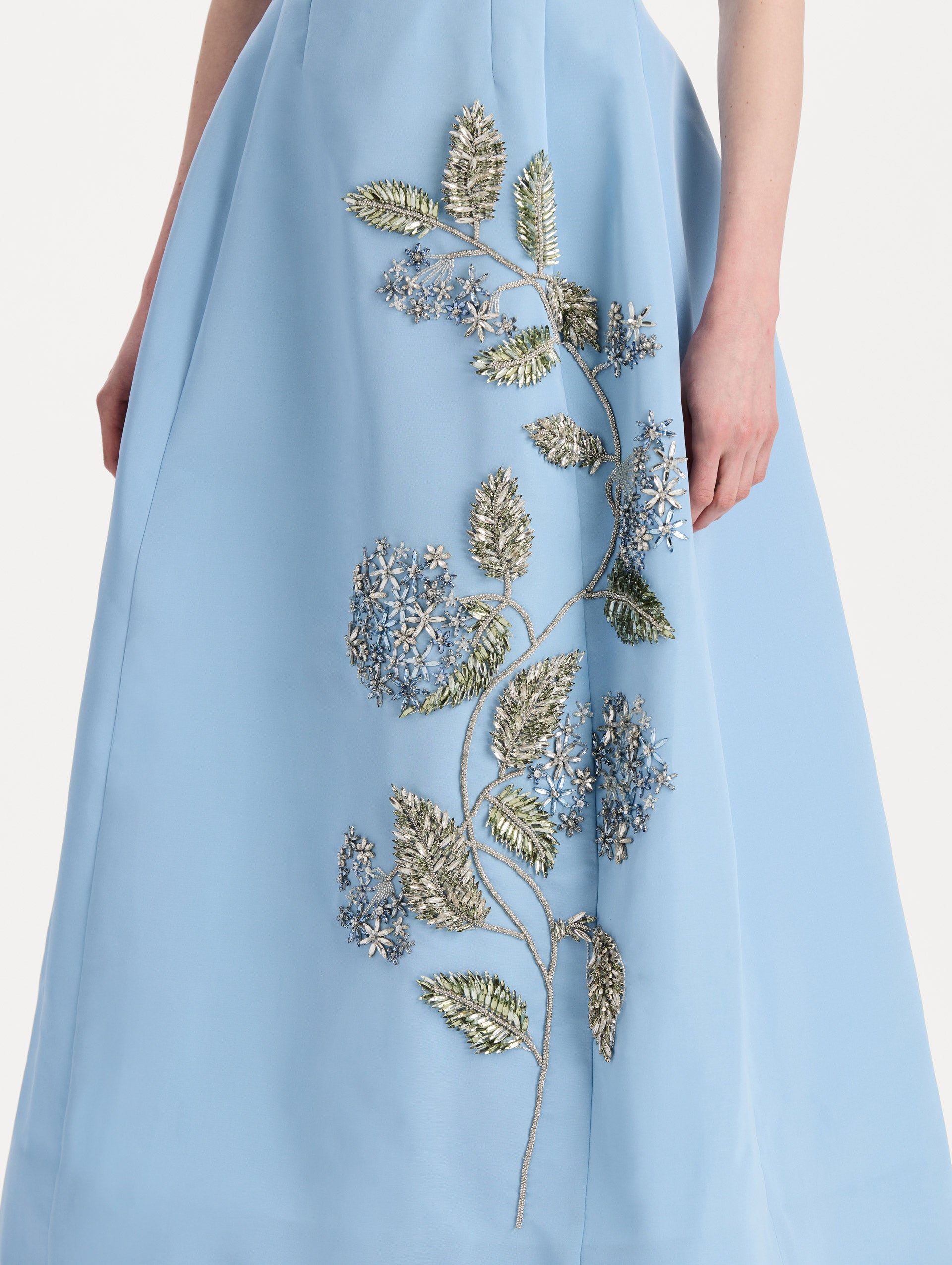 The model is wearing the Crystal Flower Embroidered Faille Dress in the color light blue with short sleeves, a sculpted skirt, and crystal-embroidered floral motifs. Detail Shot.