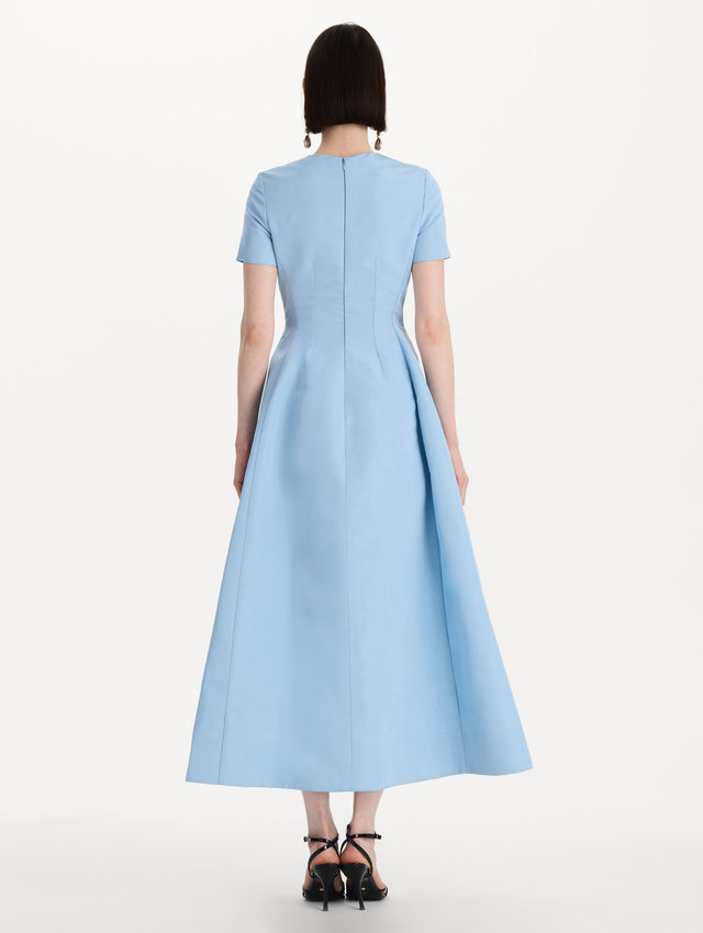 The model is wearing the Crystal Flower Embroidered Faille Dress in the color light blue with short sleeves, a sculpted skirt, and crystal-embroidered floral motifs. Back View.