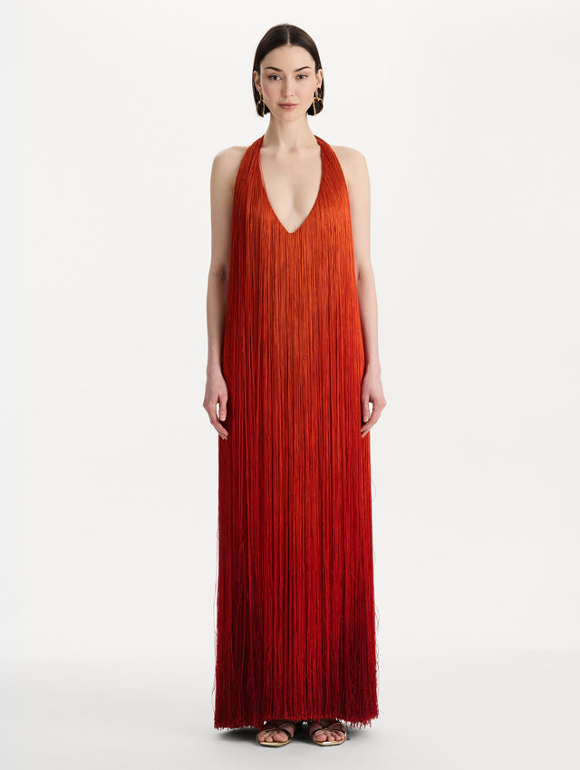 The model is wearing the Ombré Fringe Gown in Paprika Red. Featuring a deep, halter neckline, and full fringe silhouette. Front View.