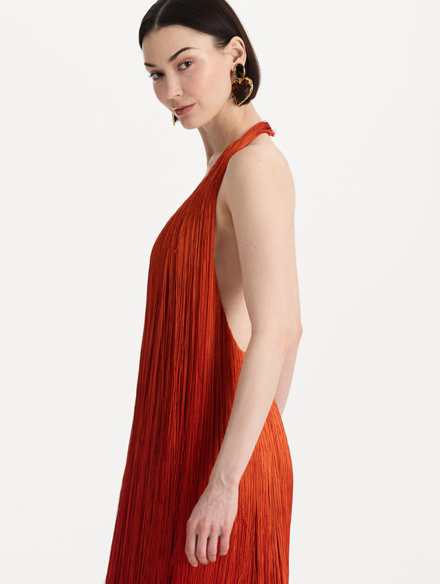 The model is wearing the Ombré Fringe Gown in Paprika Red. Featuring a deep, halter neckline, and full fringe silhouette. Detail View.