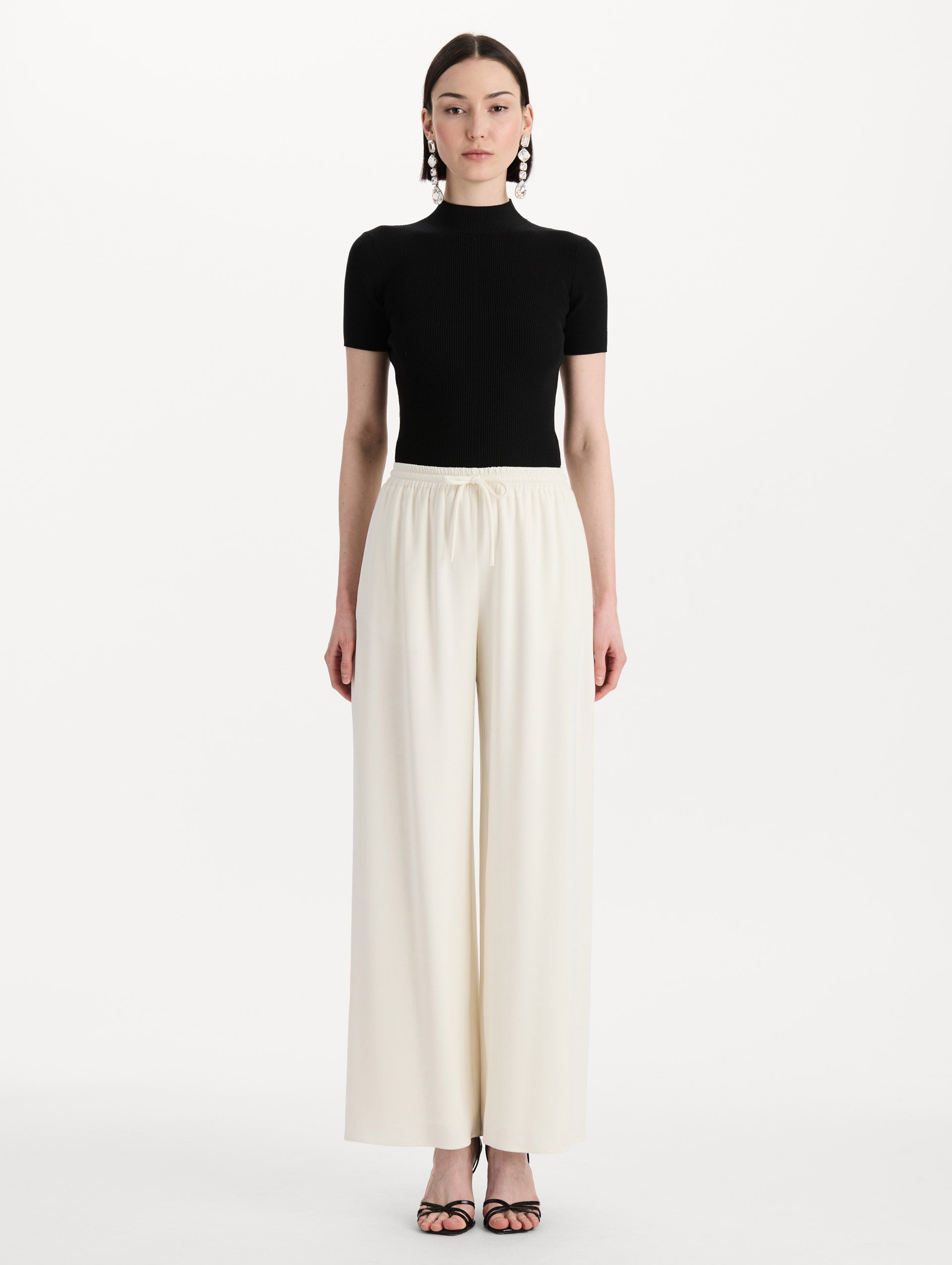 The model is wearing the Silk Georgette Drawstring Pant in the color ivory featuring straight, wide-legs and an elastic waistband finished with a drawstring tie. Front View.