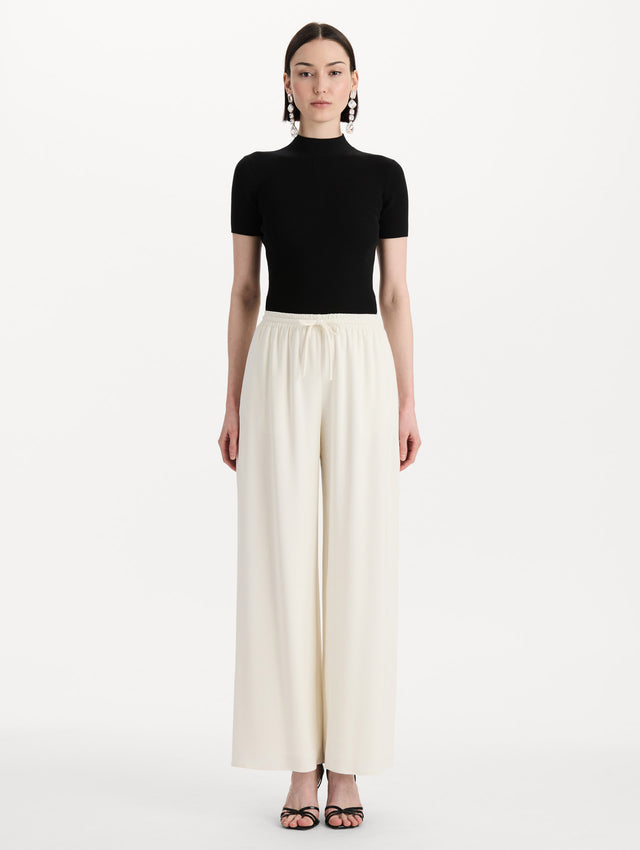 The model is wearing the Silk Georgette Drawstring Pant in the color ivory featuring straight, wide-legs and an elastic waistband finished with a drawstring tie. Front View.