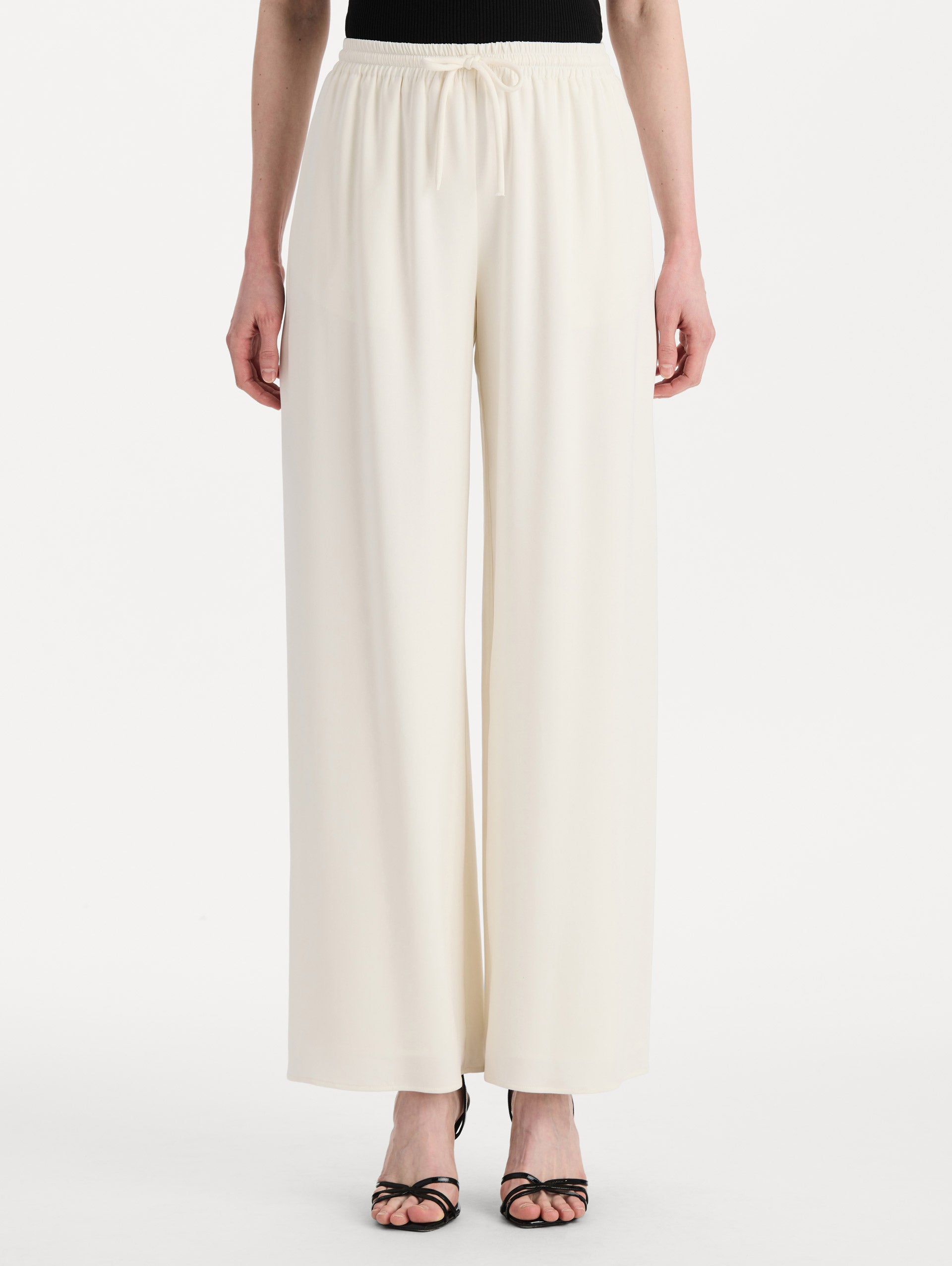 The model is wearing the Silk Georgette Drawstring Pant in the color ivory featuring straight, wide-legs and an elastic waistband finished with a drawstring tie. Front View.