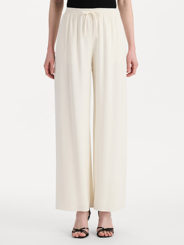 The model is wearing the Silk Georgette Drawstring Pant in the color ivory featuring straight, wide-legs and an elastic waistband finished with a drawstring tie. Front View.