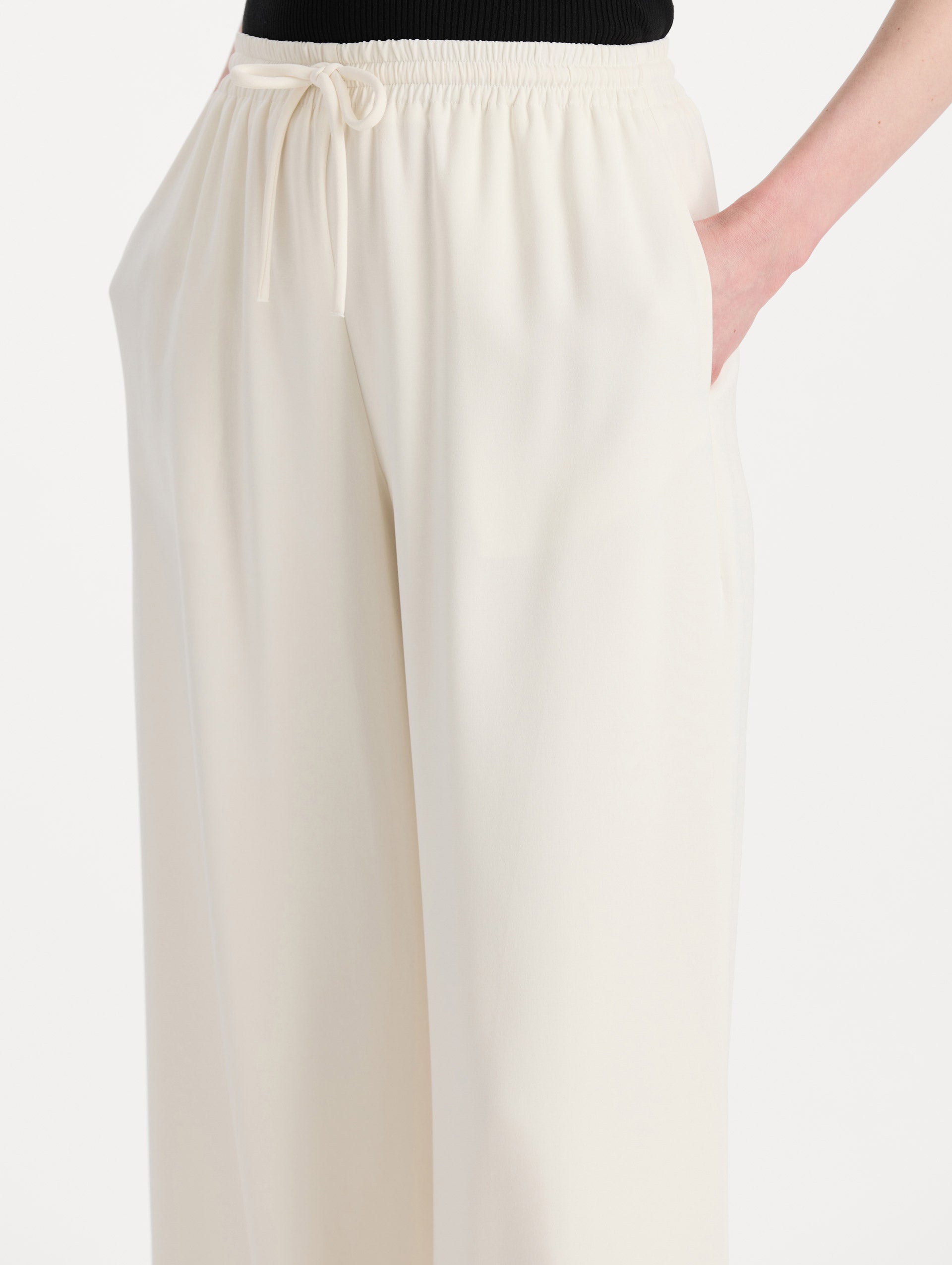The model is wearing the Silk Georgette Drawstring Pant in the color ivory featuring straight, wide-legs and an elastic waistband finished with a drawstring tie. Detail Shot.