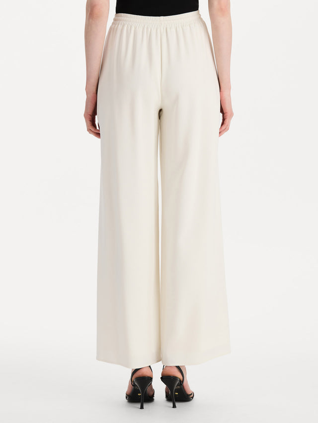 The model is wearing the Silk Georgette Drawstring Pant in the color ivory featuring straight, wide-legs and an elastic waistband finished with a drawstring tie. Back View.