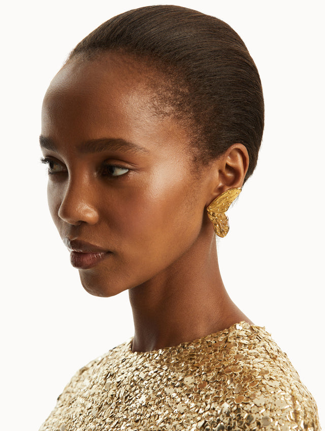 The model is wearing a gold butterfly wing earring, paired with a gold gown. Front view.