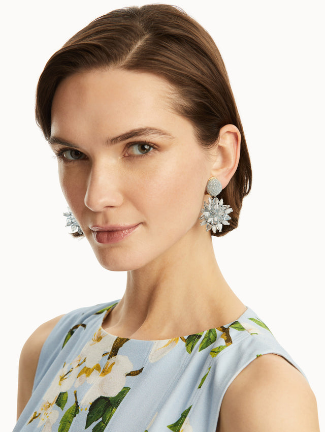 The model is wearing blue beaded flower earrings with raffia detailing. Front view.