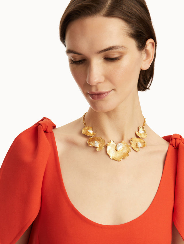 The model is wearing a gold chain-link necklace, with gold lily pads and a pearl at the center of each. Front view.