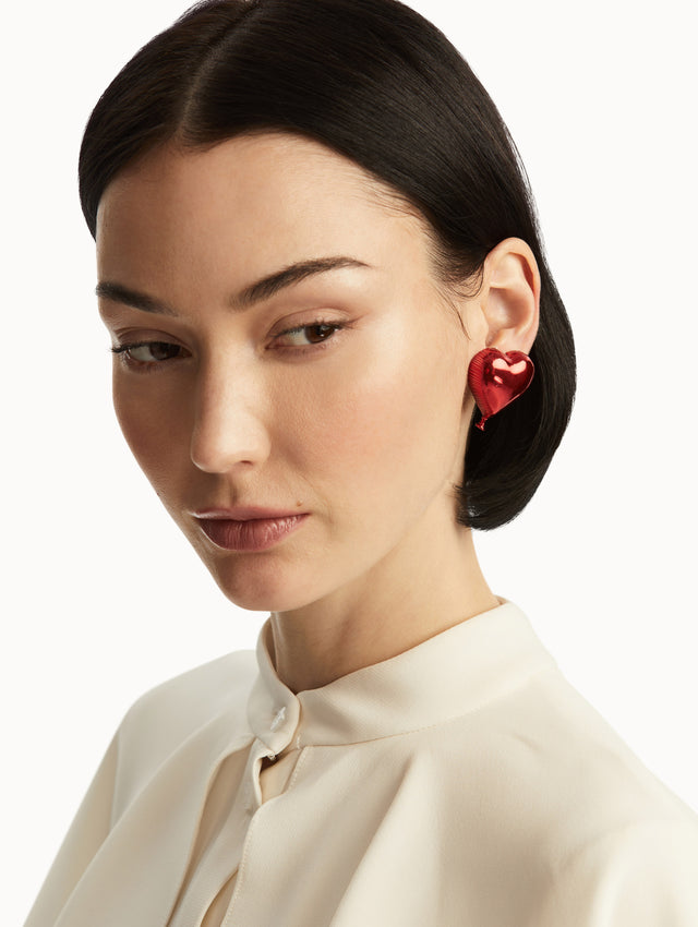 The model is wearing red metallic heart balloon earrings, paired with a white blouse. Front view.