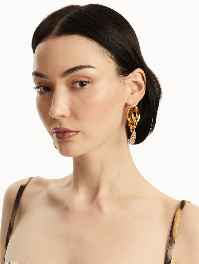 Model is wearing interlocking O gold knot earrings with a pave crystal drop in the bottom Front view