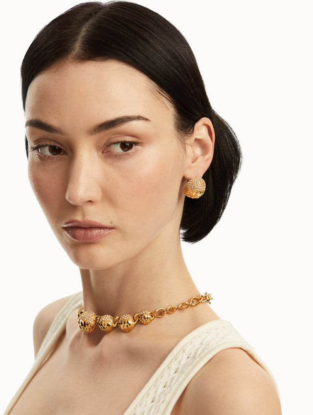 The model is wearing gold, artichoke inspired earrings with crystals on the top part, paired with a matching necklace. Front view