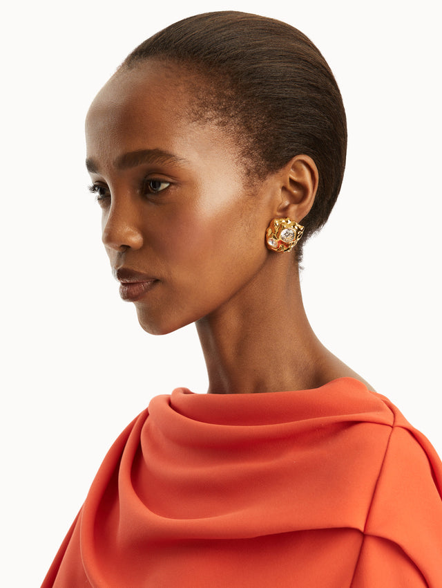 the model is wearing gold textured earrings embedded with two crystals and paired with a red gown. Front view