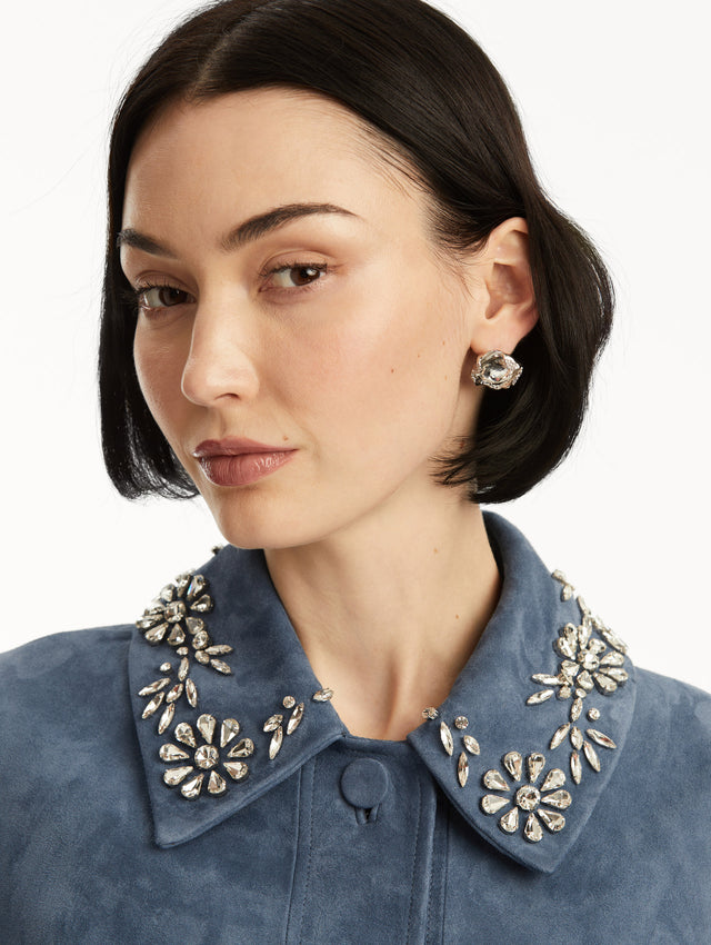 The model is wearing a textured silver stud with a crystal in the center, paired with a blue suede jacket. Front view