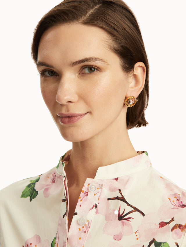 The model is wearing gold textured studs with a pink crystal in the center, paired with a cherry blossom dress. Front view