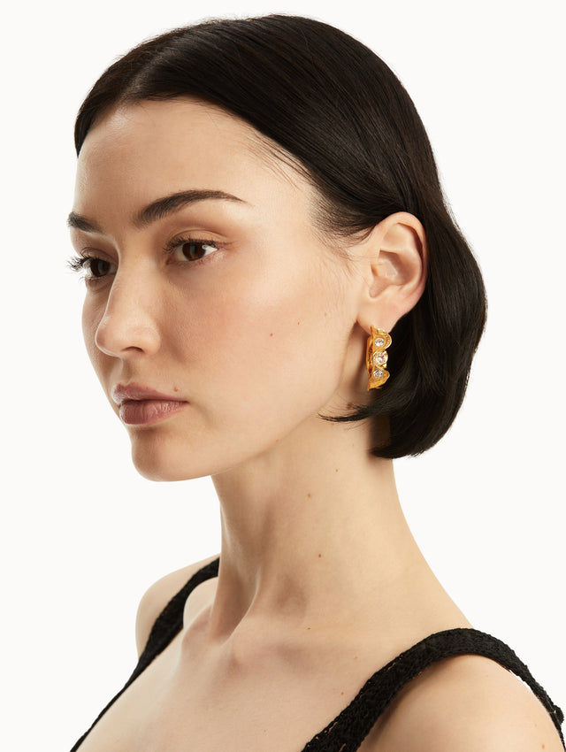 The model is wearing gold hoop earrings with texture and 3 crystals. Front view
