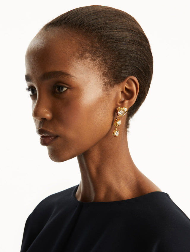 The model is wearing three-tier drop down earrings in gold, with a crystal in each tier. Front view