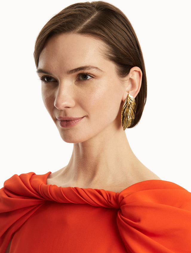 The model is wearing large gold leaf earrings paired with a red gown. Front View