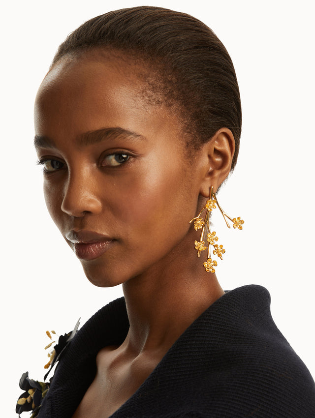 The model is wearing gold branch earrings with cherry blossoms, paired with a black sweater. Front view
