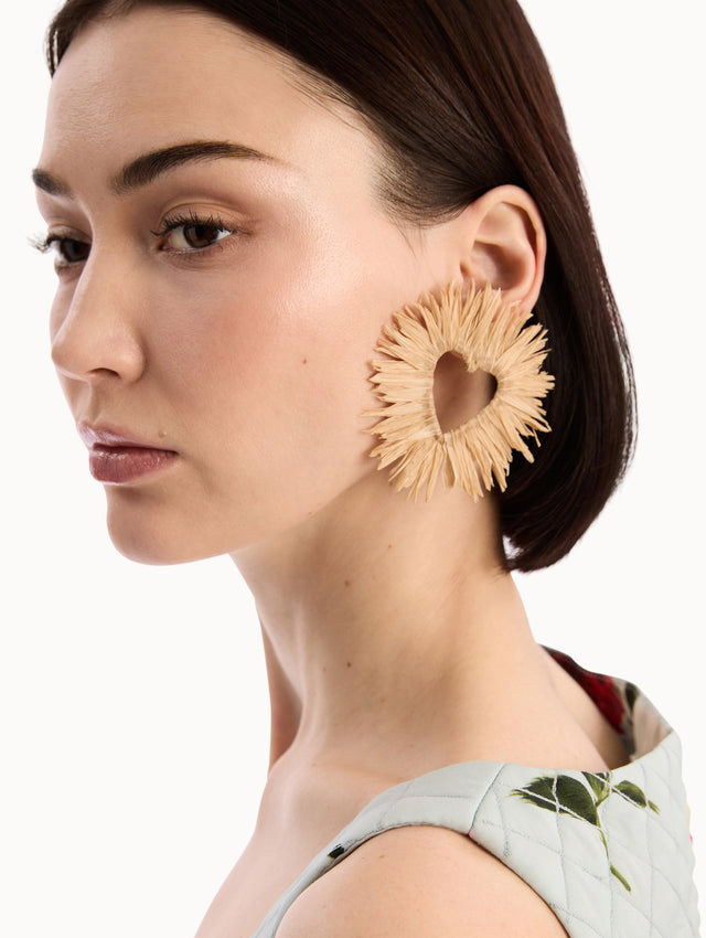 The model is wearing the Raffia Heart Earrings with heart cut-out center. Detail View.