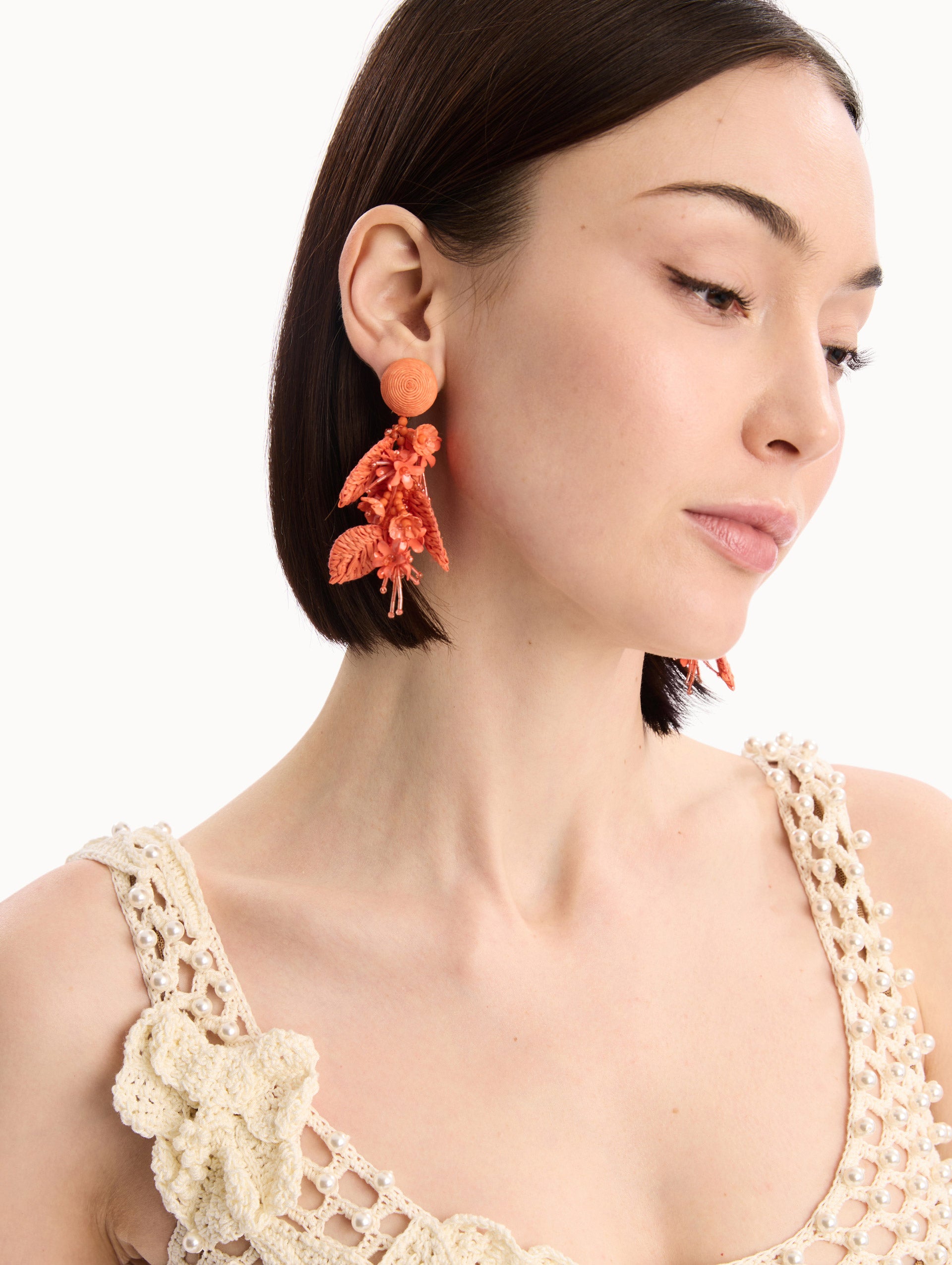 The model is wearing the Raffia Tassel Bouquet Clip-On Earrings in Orange. Detail View.