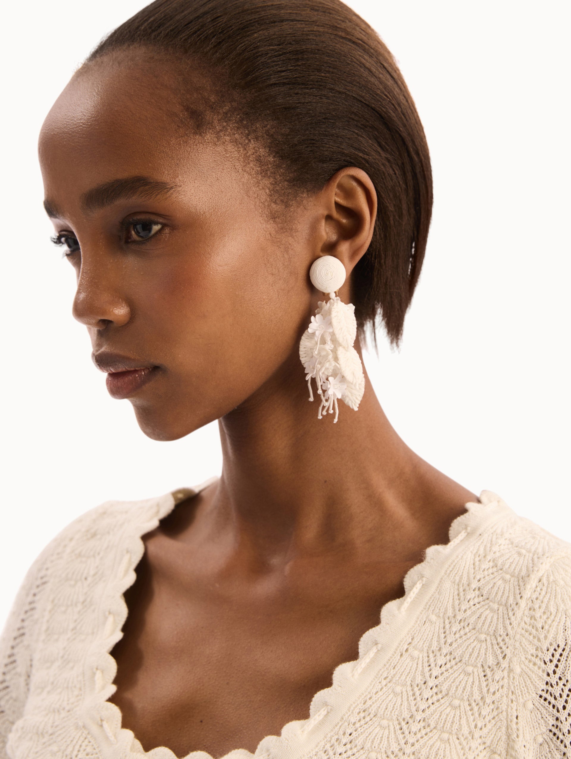The model is wearing the Raffia Tassel Bouquet Clip-On Earrings in White. Detail View.