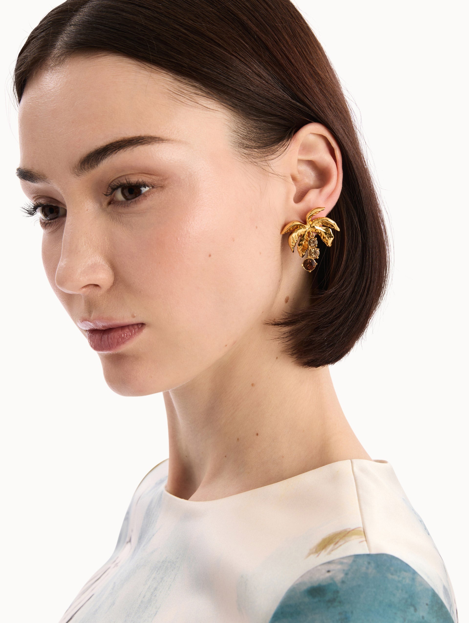 The model is wearing the Palm Leaf Clip-On Earrings in Gold with Crystal Trunks. Detail View.