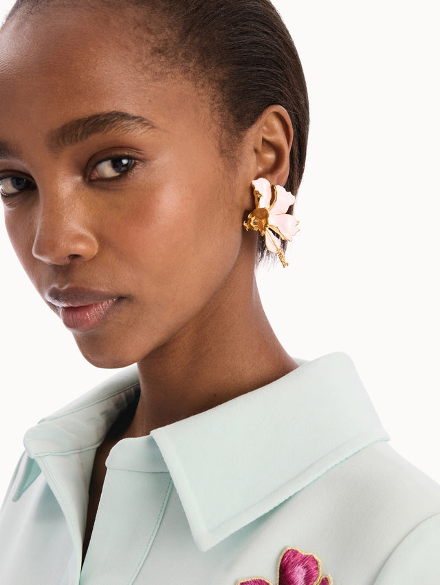 The model is wearing the Enamel Folded Hibiscus Clip-On Earrings in Light Pink. Detail View.