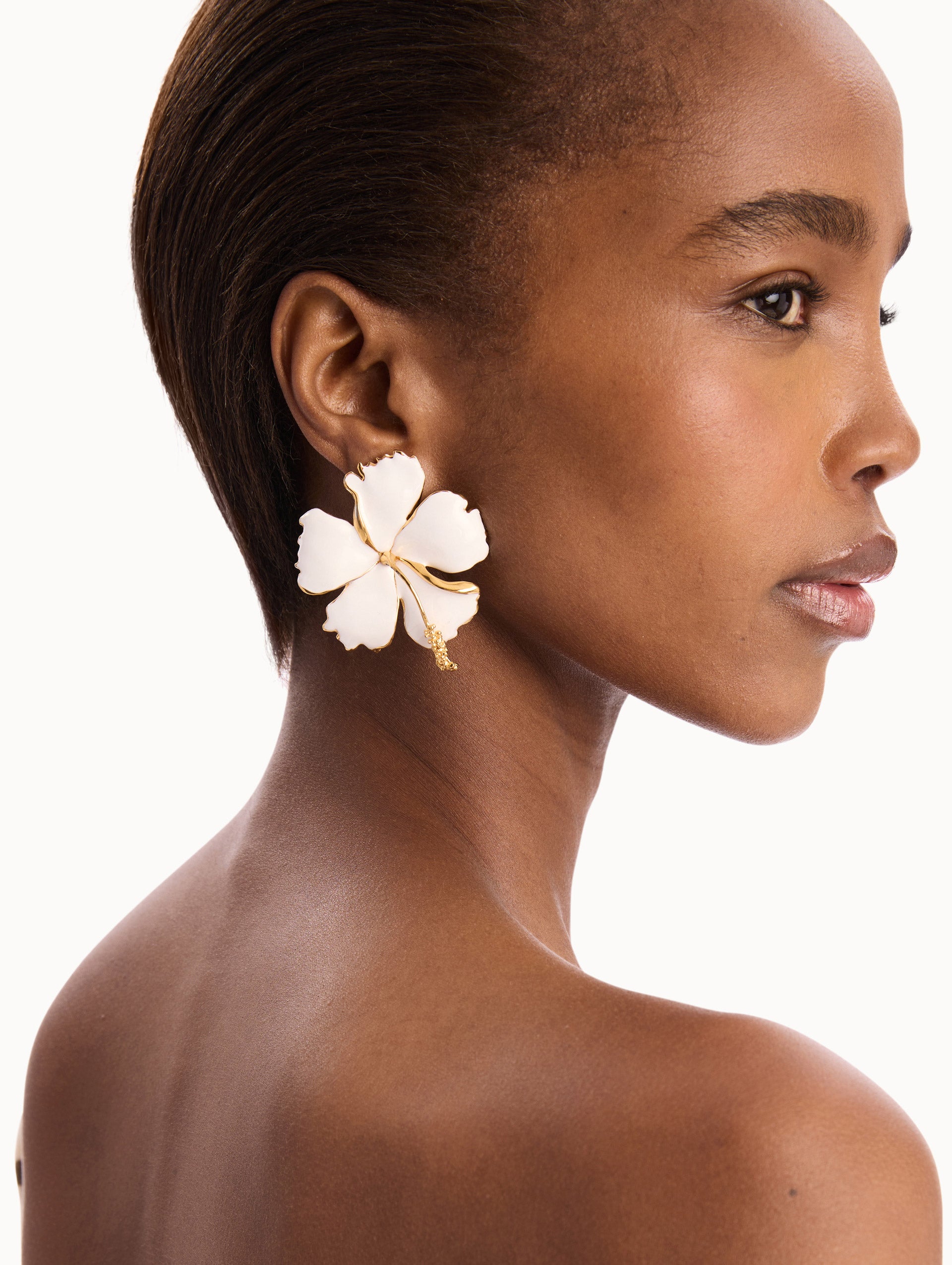 The model is wearing the Enamel Hibiscus Clip-On Earrings in White. Detail View.