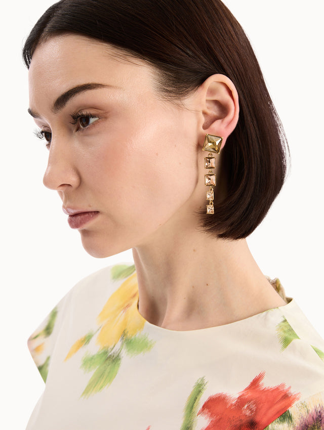 The model is wearing the Square-Cut Rhinestone Drop Earrings in Gold. Detail View.