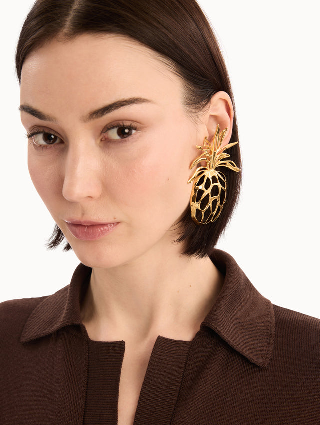 The model is wearing The Openwork Pineapple Clip-On Earrings. Gold Pineapple-shaped Silhouette. Detail View.