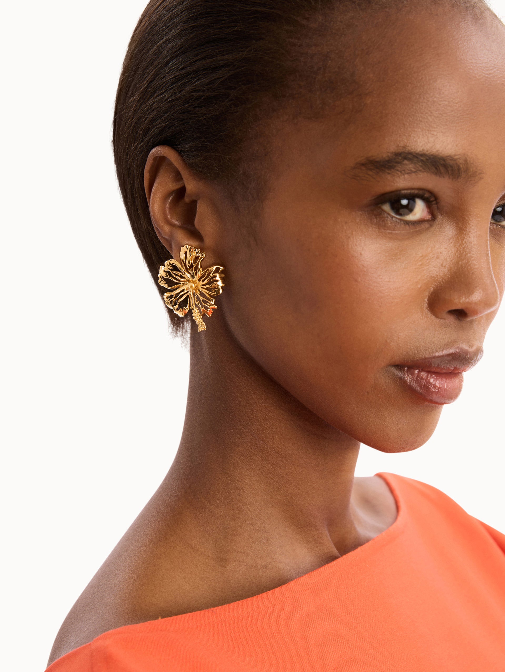 The model is wearing the Openwork Hibiscus Earrings in Gold. Detail View.